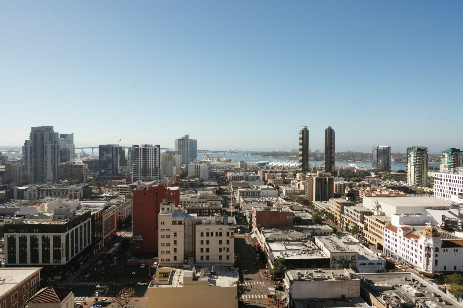 View from an upper floor over downtown rooftops toward the bay, a bridge and the white roof of the convention center
