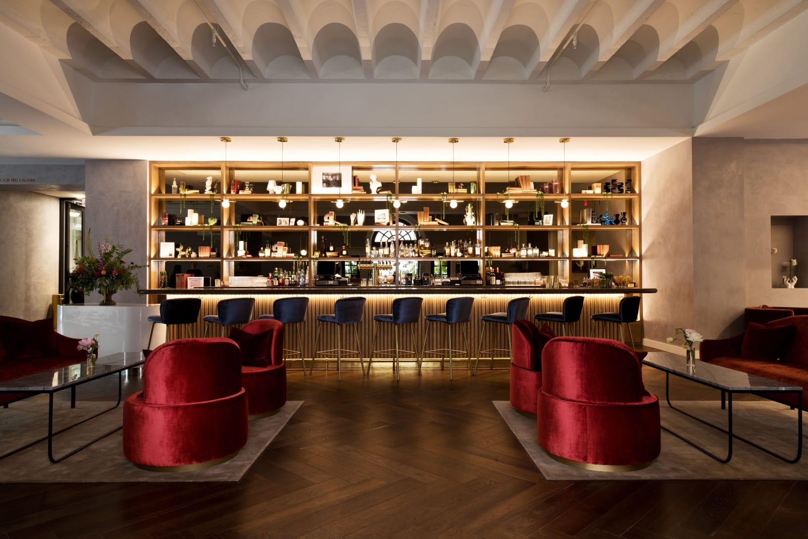 Bar area with round red velvet chairs and a lit wall of bottles behind
