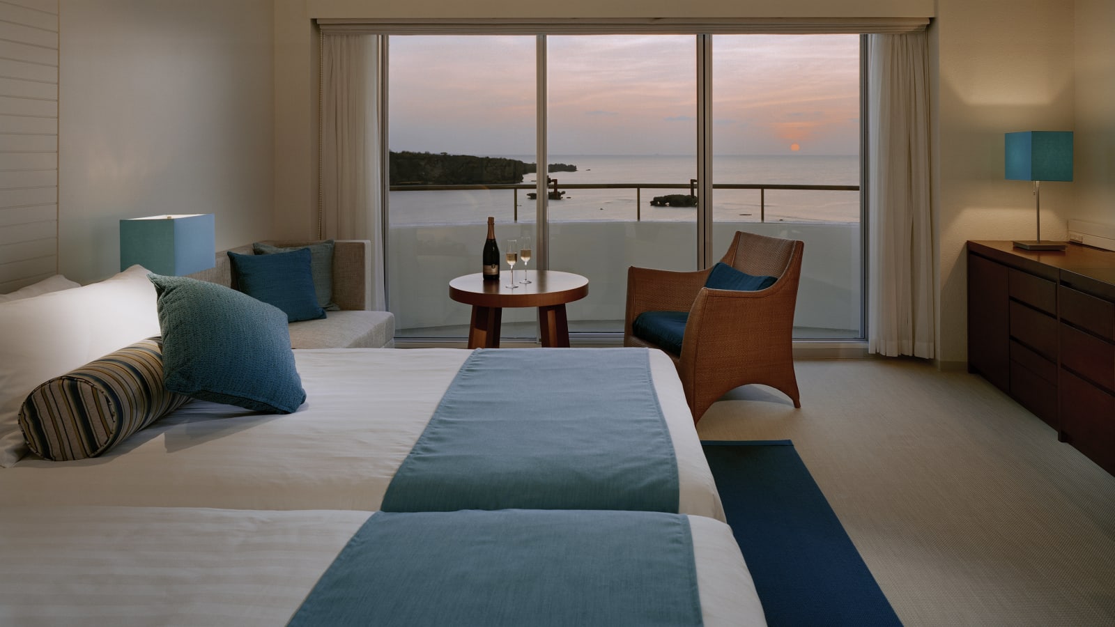 Standard guest room in white and blue with twin beds and a balcony beyond the glass doors