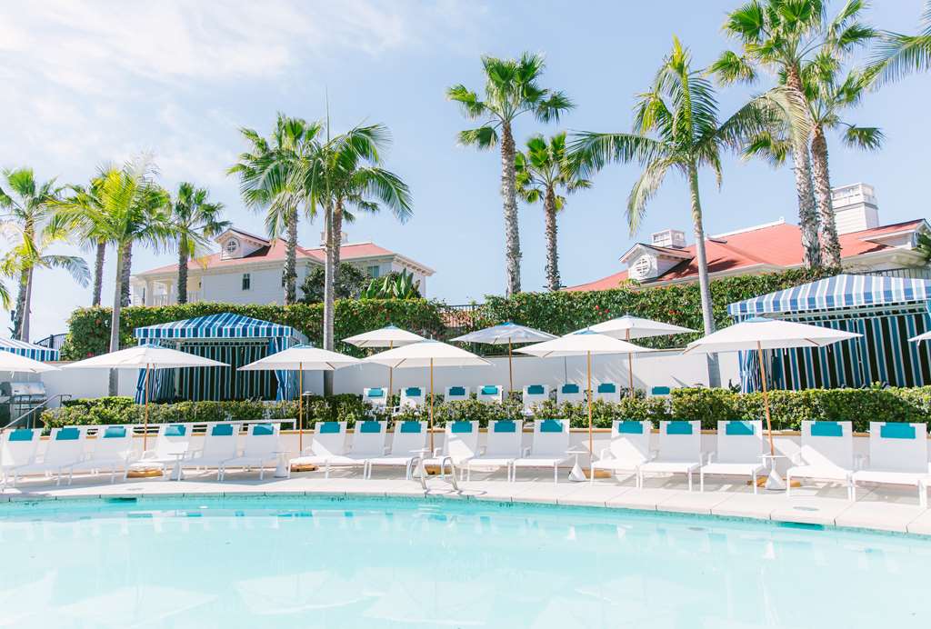 Poolside row of striped cabanas and white umbrellas with palms and red roofs behind