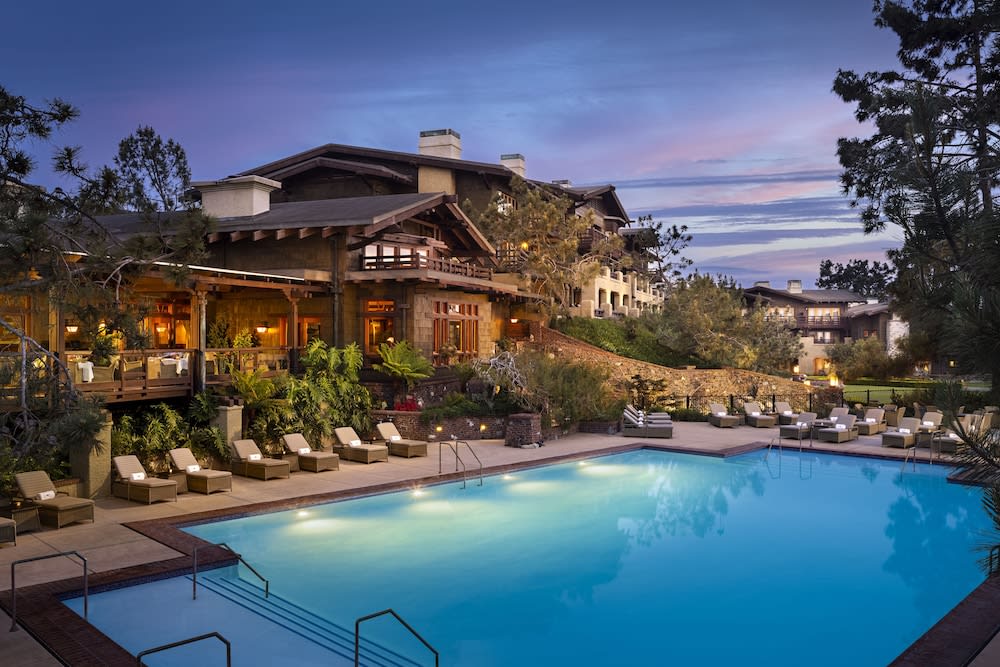 Timber lodge exterior at dusk with a lit swimming pool in front