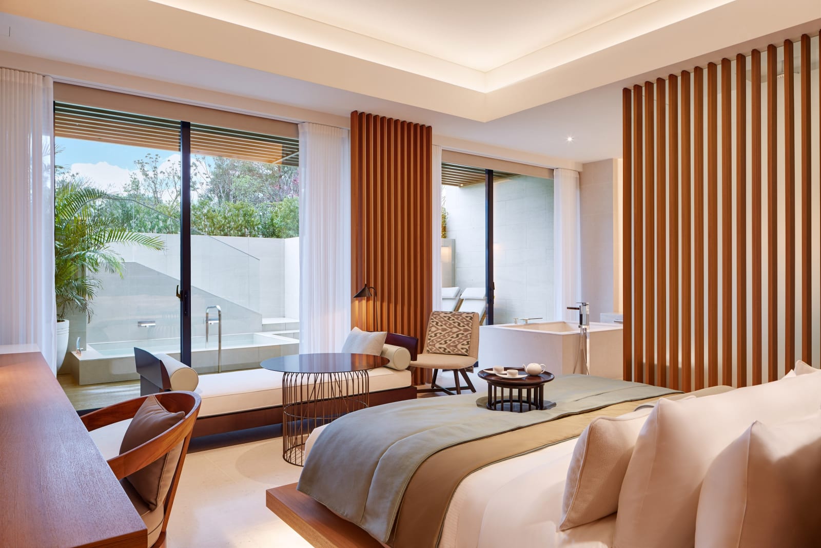 A guest room bed beside floor-to-ceiling doors onto a balcony