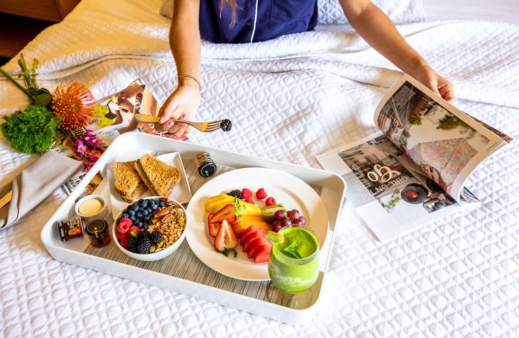 Breakfast tray on a bed with pastries, berries, yoghurt and juice