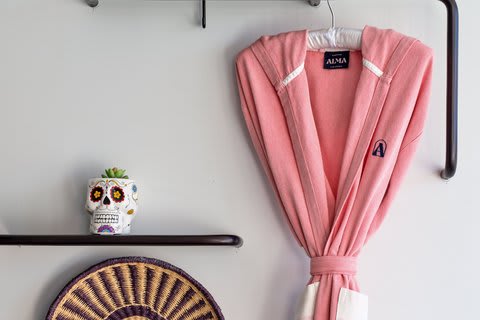 Pink robe embroidered with ALMA hanging on a white wall above a painted skull ornament