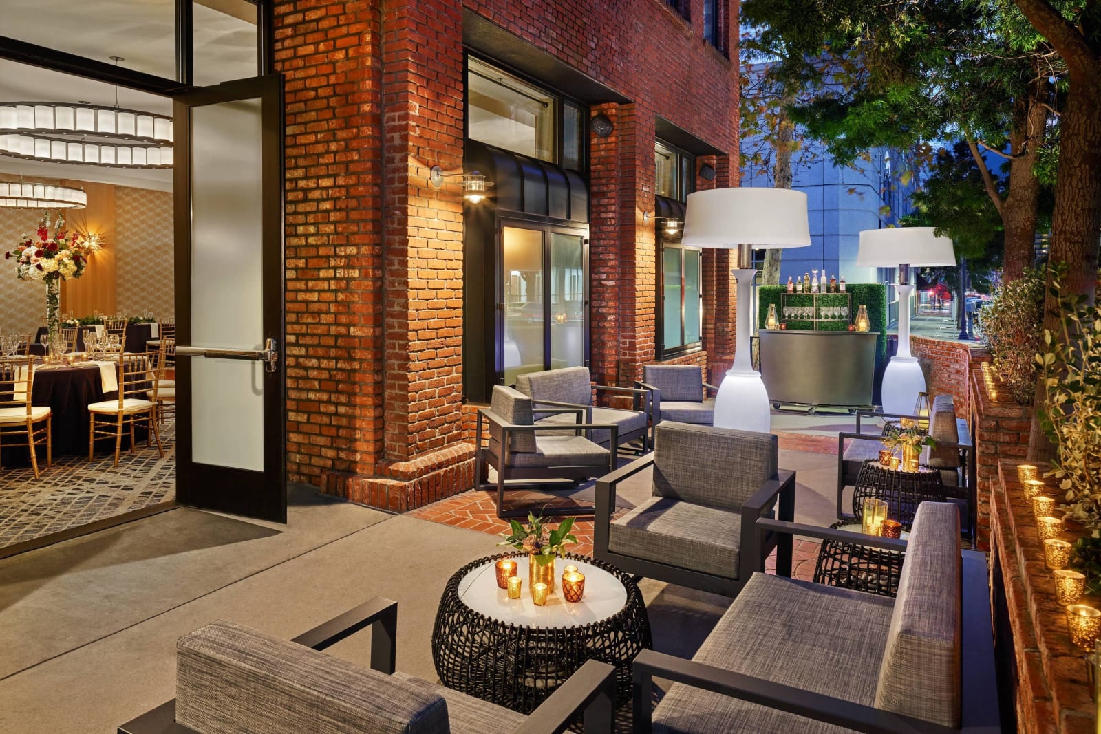 Brick walled walkway at night with a fire table, armchairs and strings of bulbs