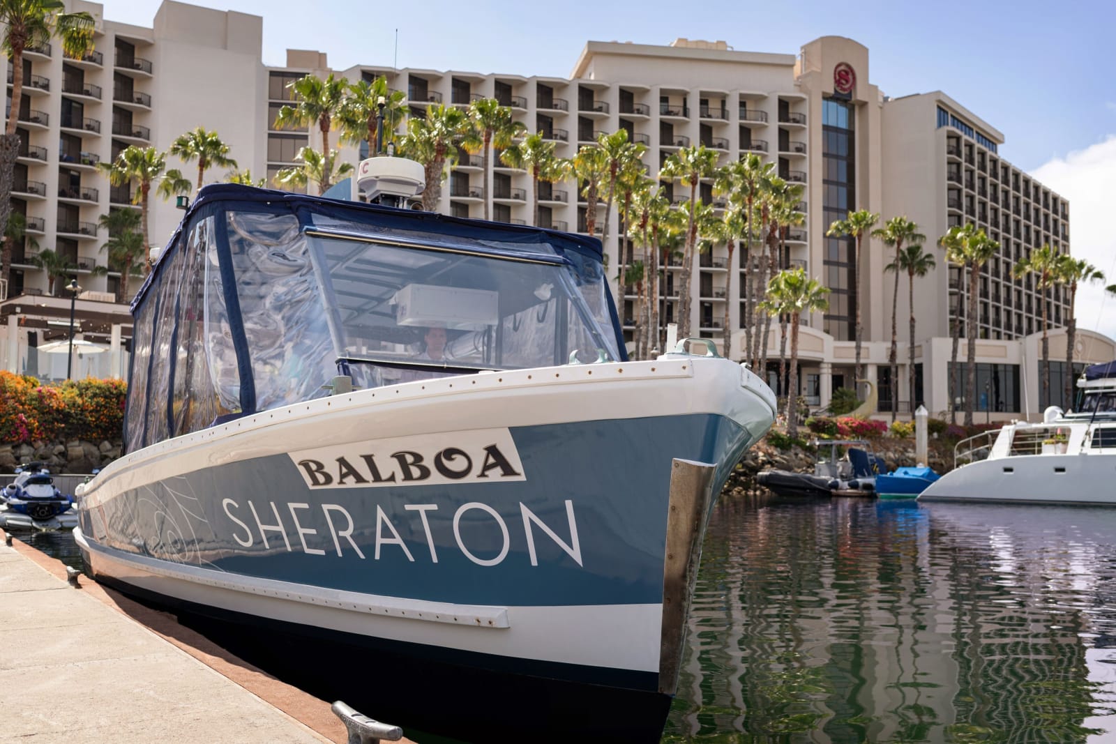 A blue and white excursion boat moored at the marina with the hotel name on its hull