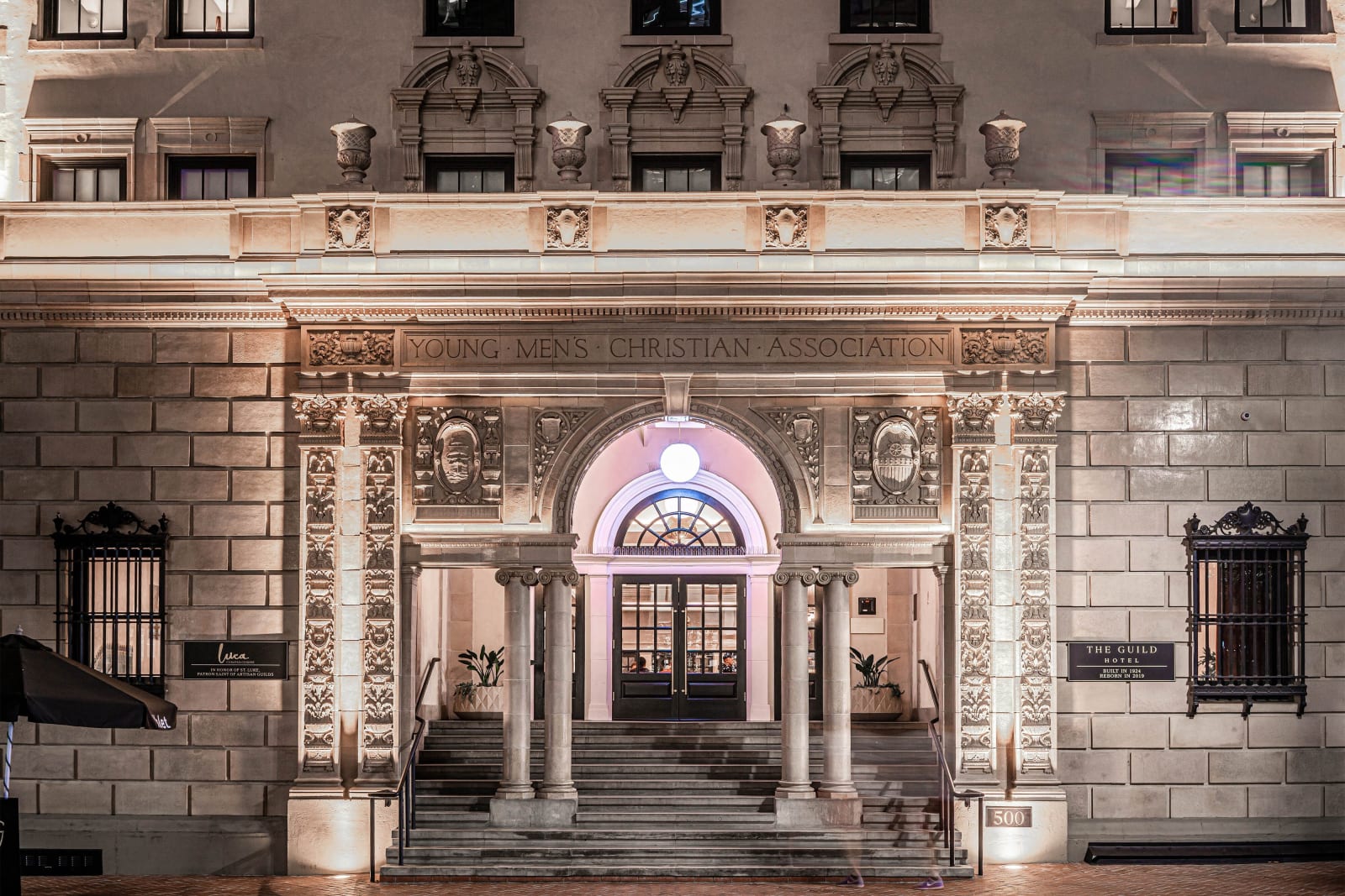 Ornate stone historic facade with an arched doorway above a flight of steps flanked by rails