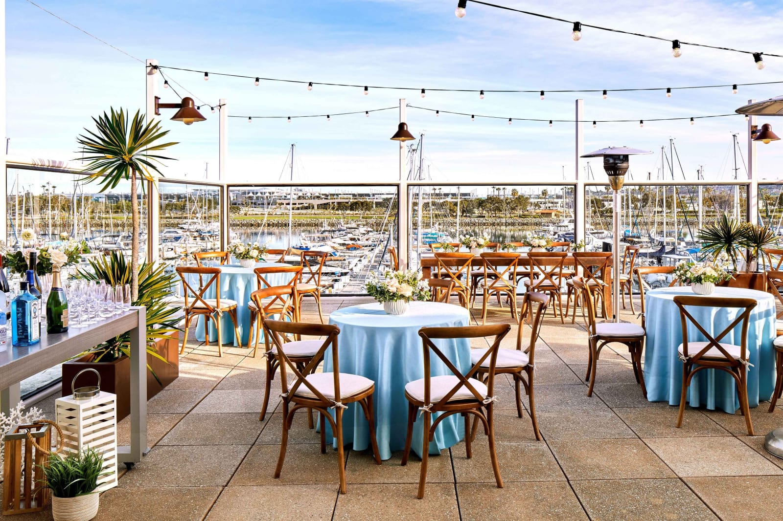 Open air deck with round tables and string lights, marina beyond the railing