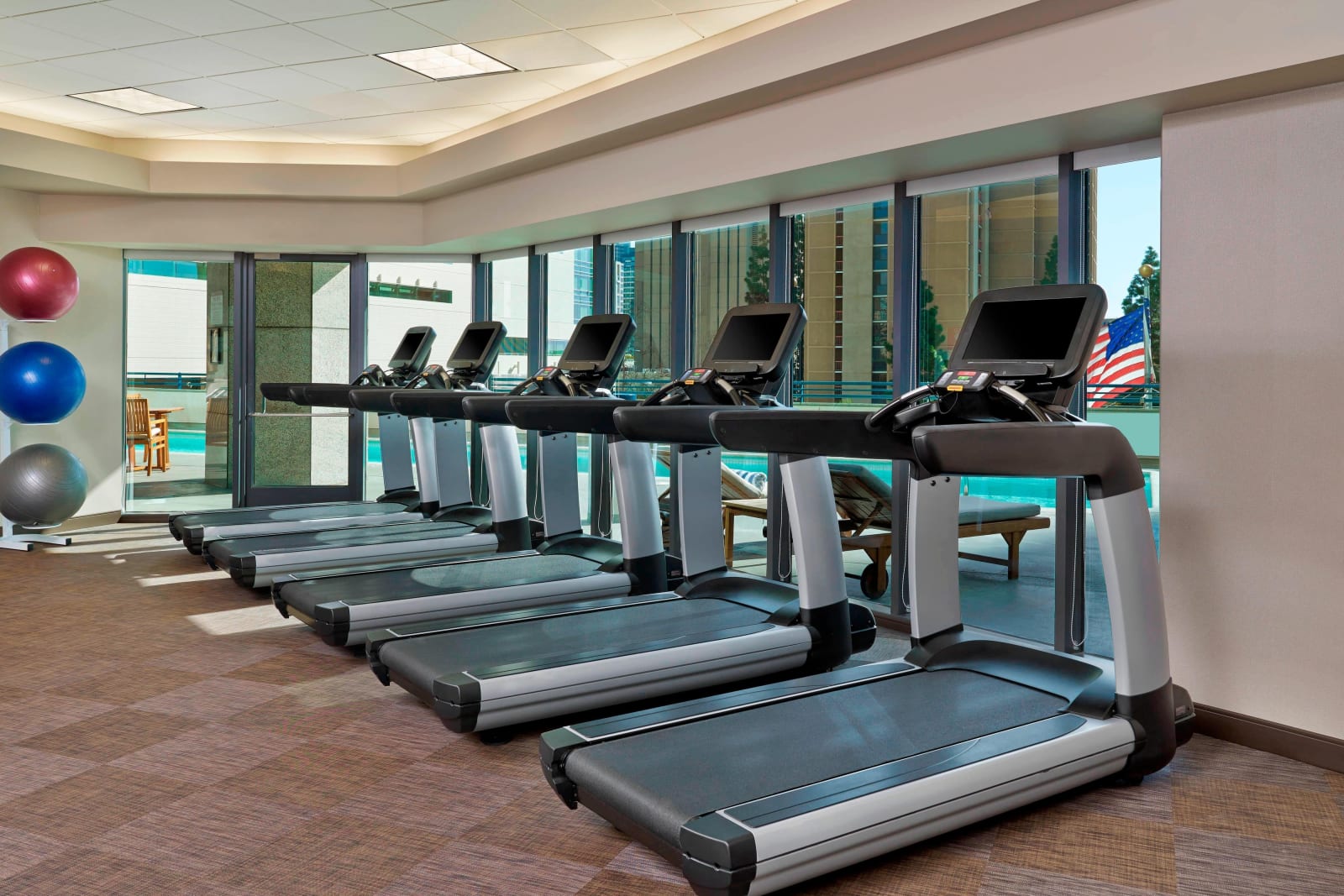 Row of treadmills in a hotel gym facing a wall of windows