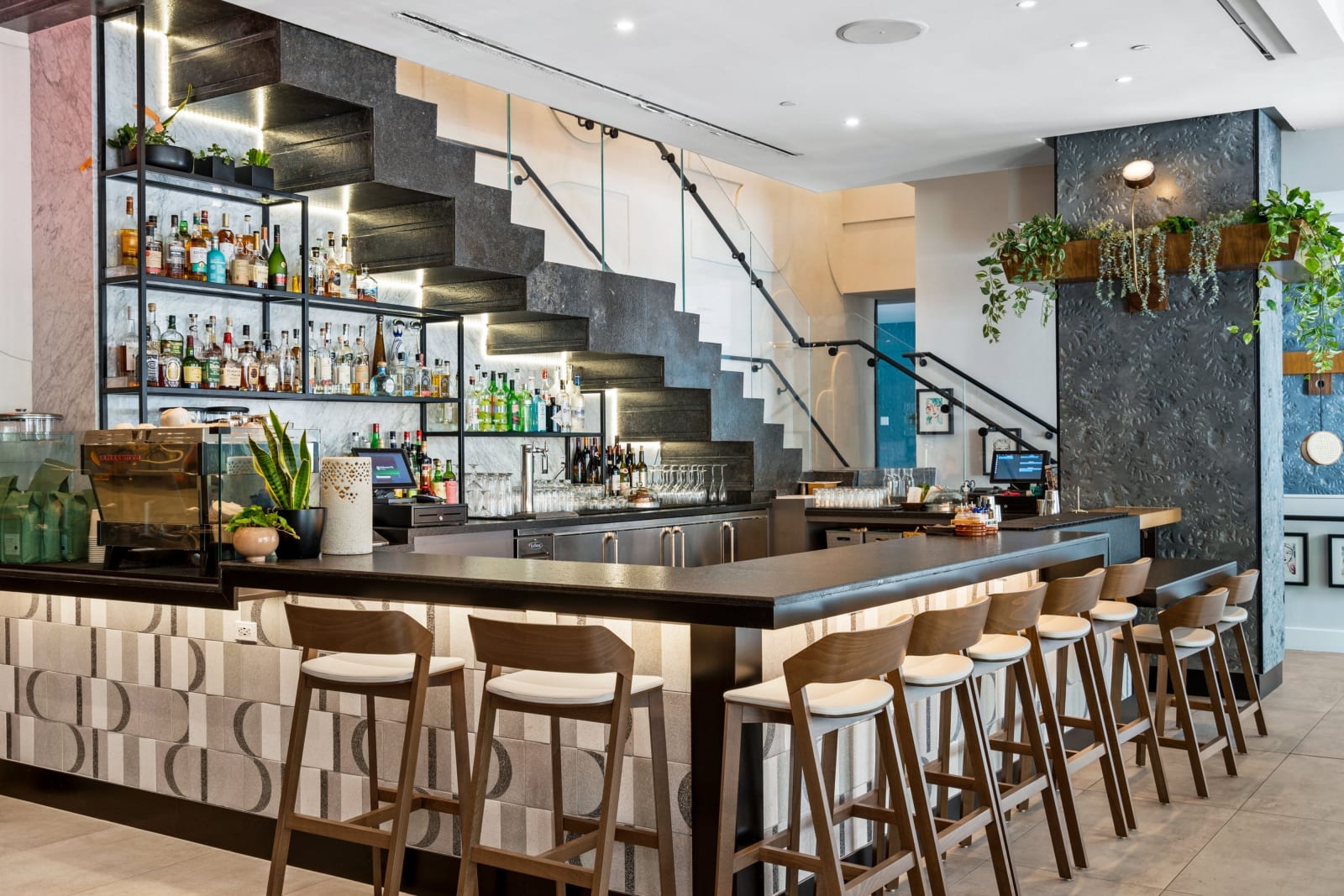 Long bar counter with stools, a dark stone staircase behind it and hanging green plants above