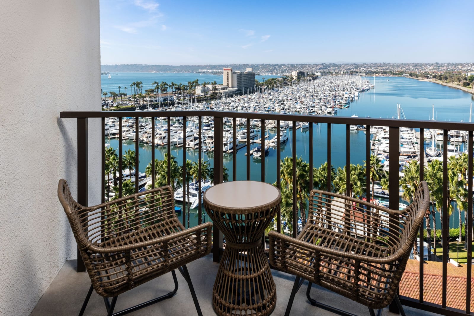 Guest balcony with woven furniture, marina and skyline beyond the railing
