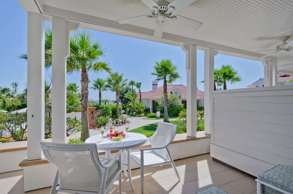 Covered porch on white columns with woven table and chairs, lawn and palms beyond
