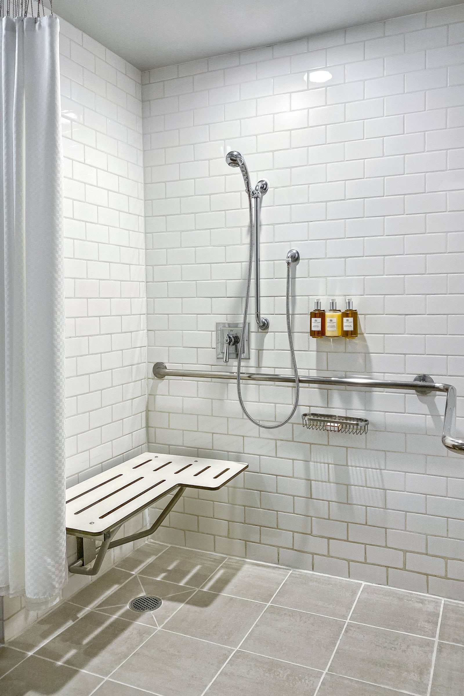 Accessible shower with horizontal grab bars and a fold down seat against white tile
