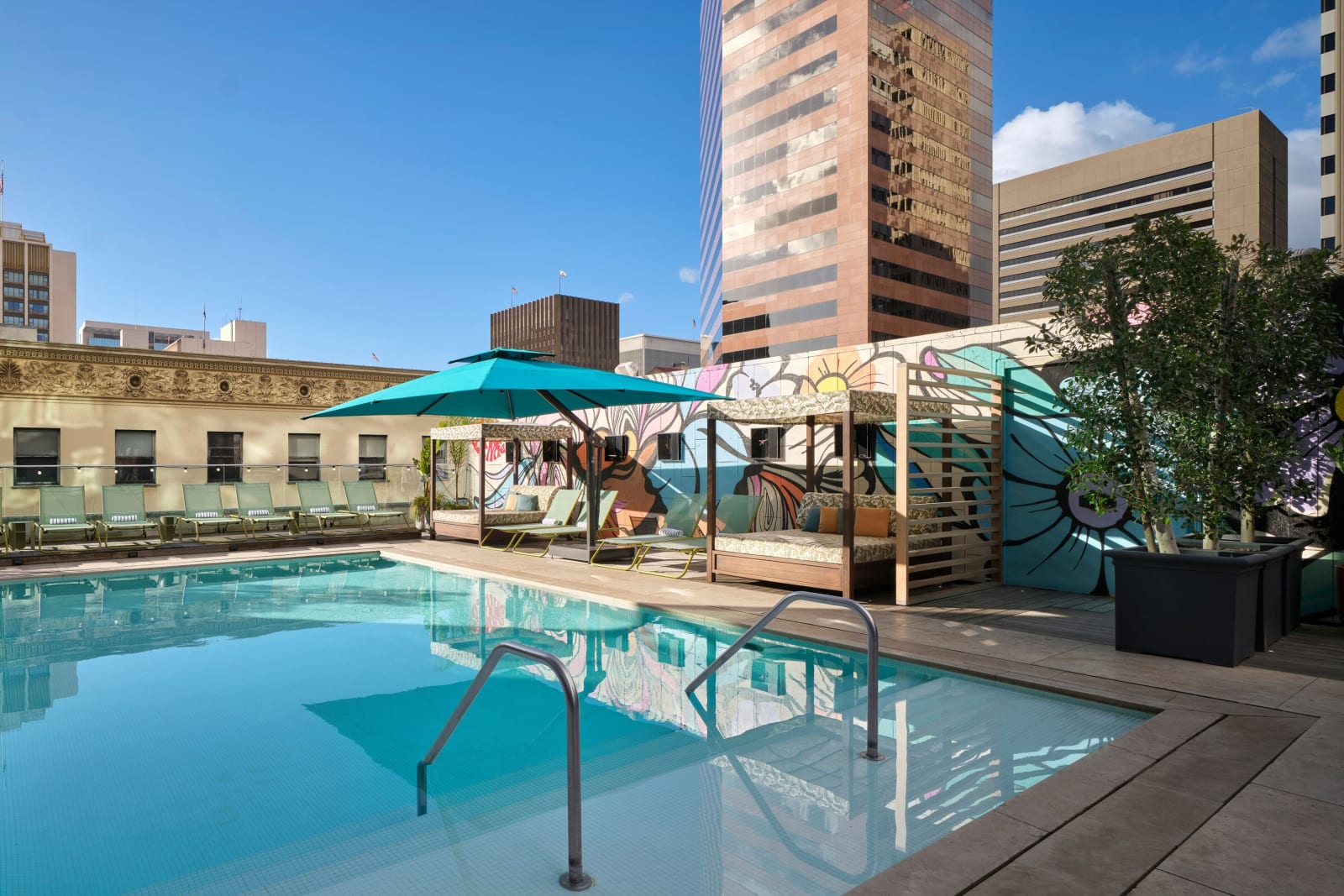Rooftop pool with bright water, a painted mural along the far wall and downtown office towers behind