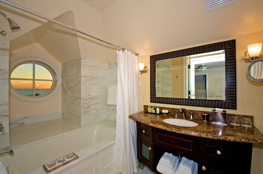 Bathroom with a tub below a round porthole window and a dark wood vanity alongside