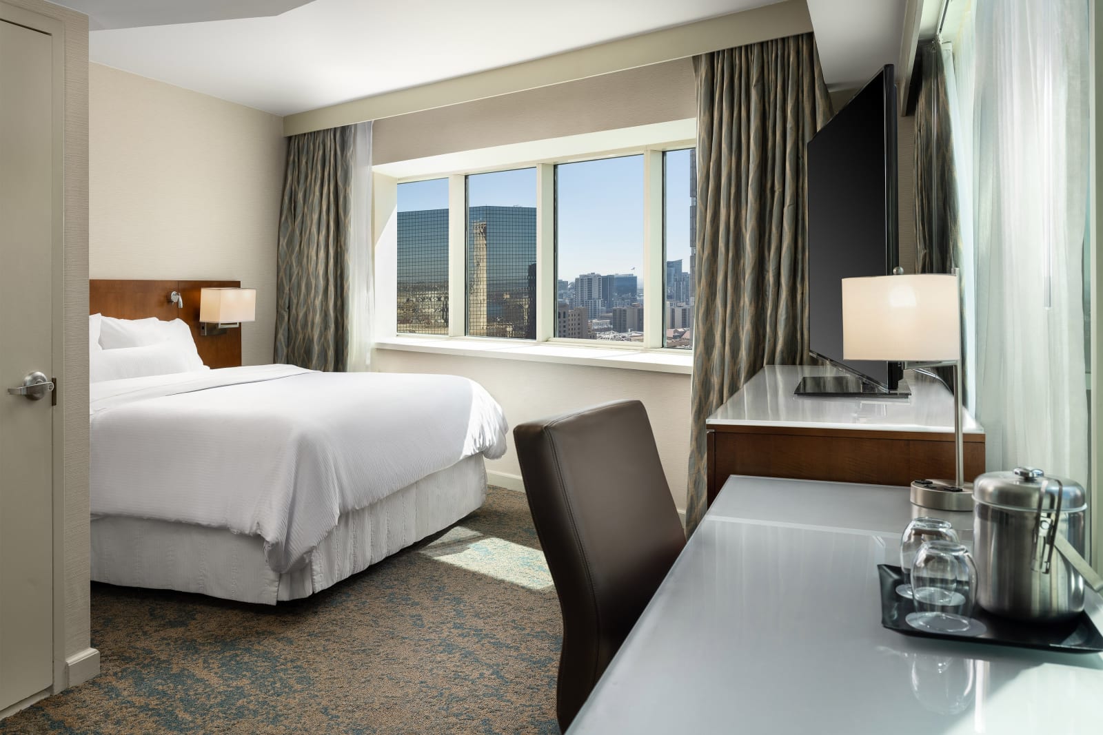 Renovated guest room with a king bed and a full height window onto the city