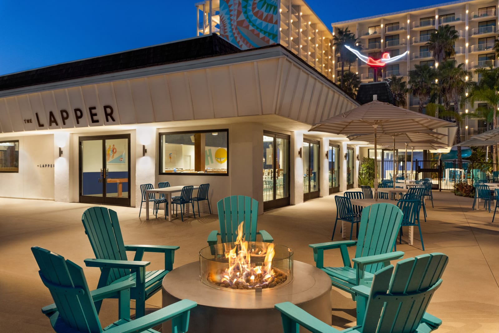 Restaurant exterior at dusk with a fire pit and teal Adirondack chairs in front