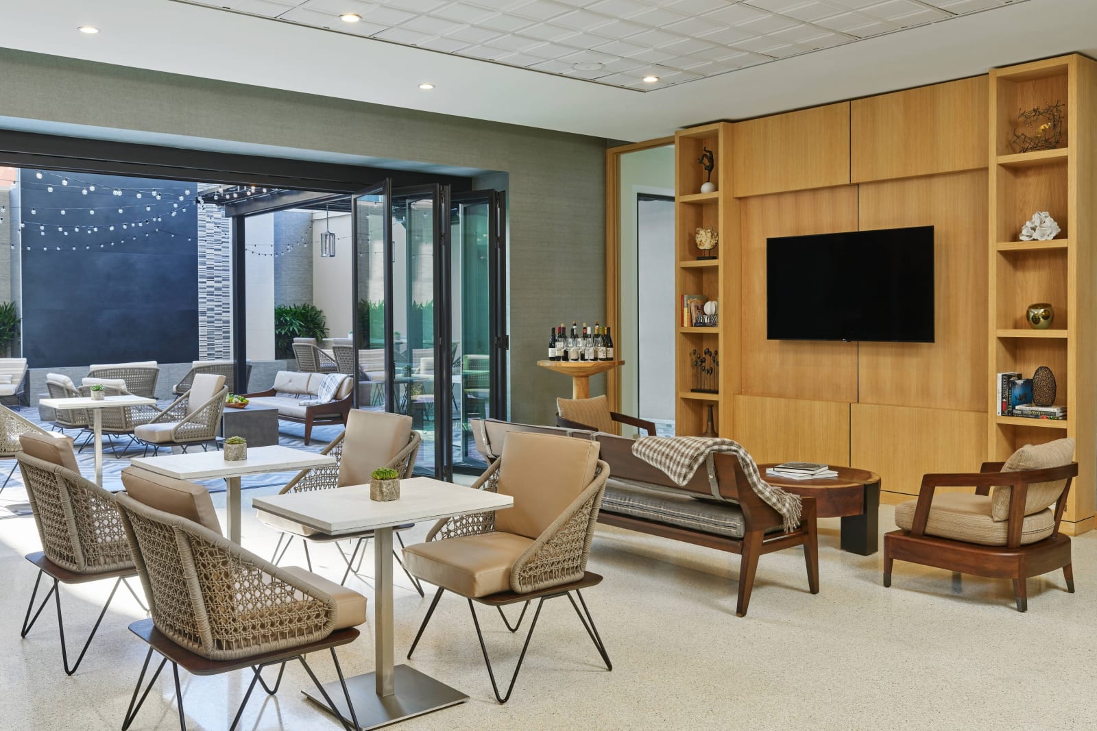 Bright lounge with wooden shelving, small white tables and glass doors to a terrace