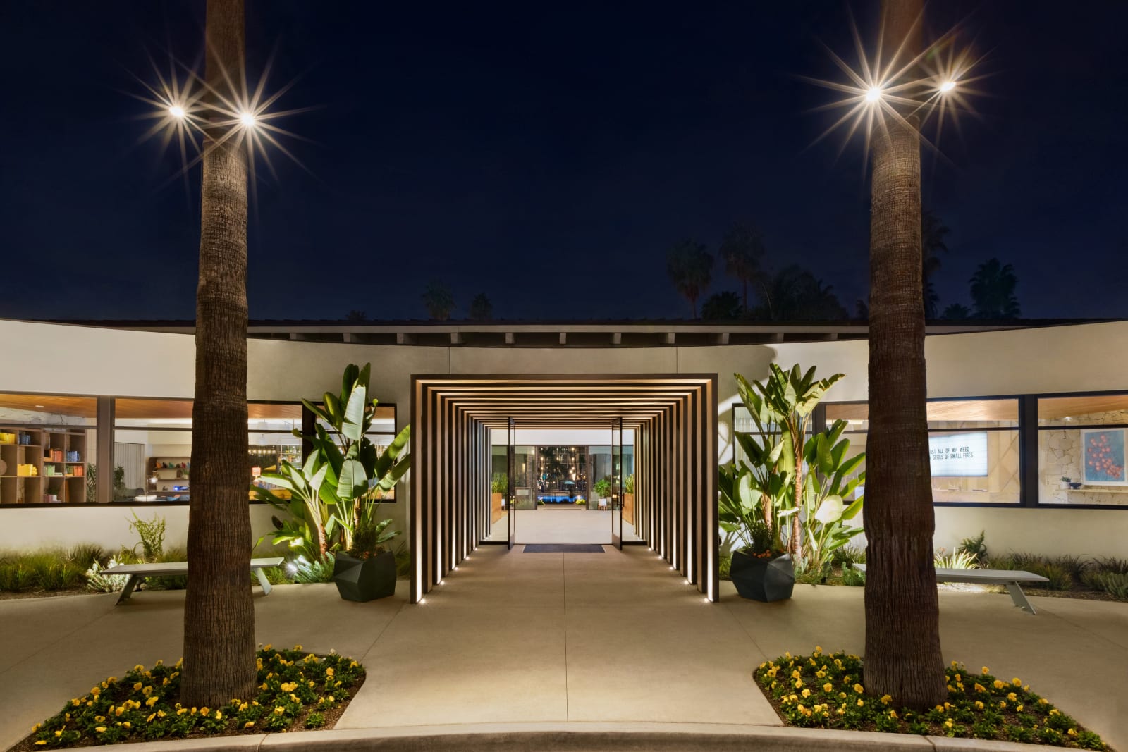 Arrival colonnade at night with rows of lamp posts and palms leading to a lit portico