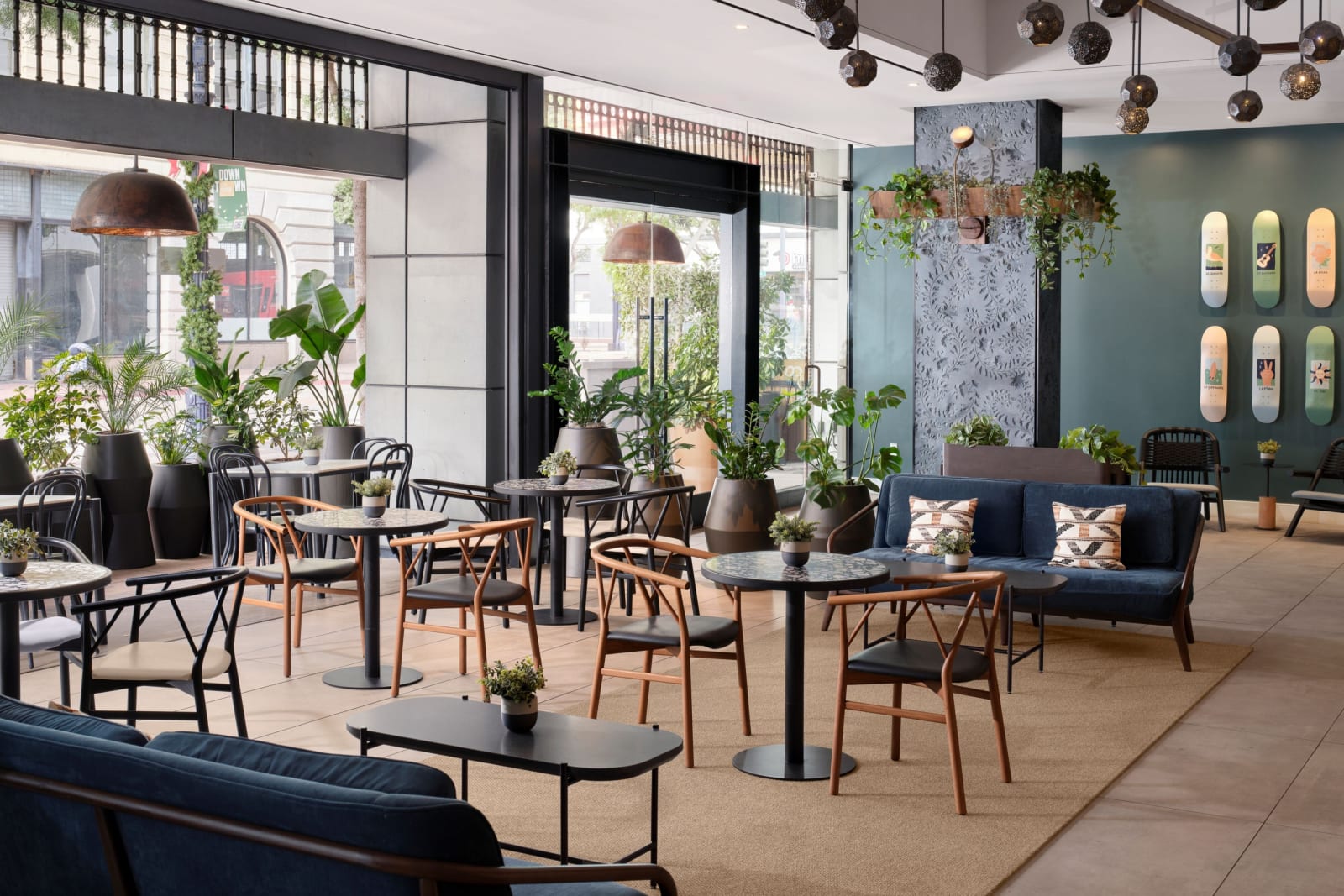 Ground floor restaurant with deep blue banquettes, round wooden tables, heavy planting and full height windows onto the street