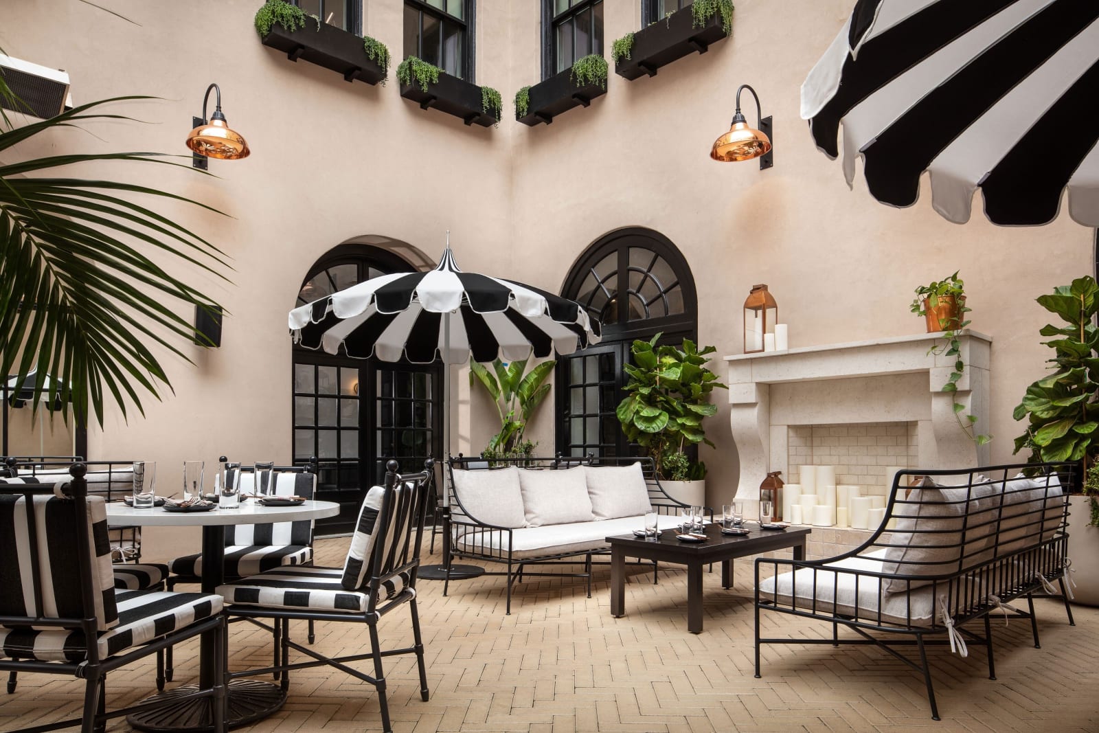 Courtyard with black and white striped awnings, arched windows, a fireplace and palms against pink walls