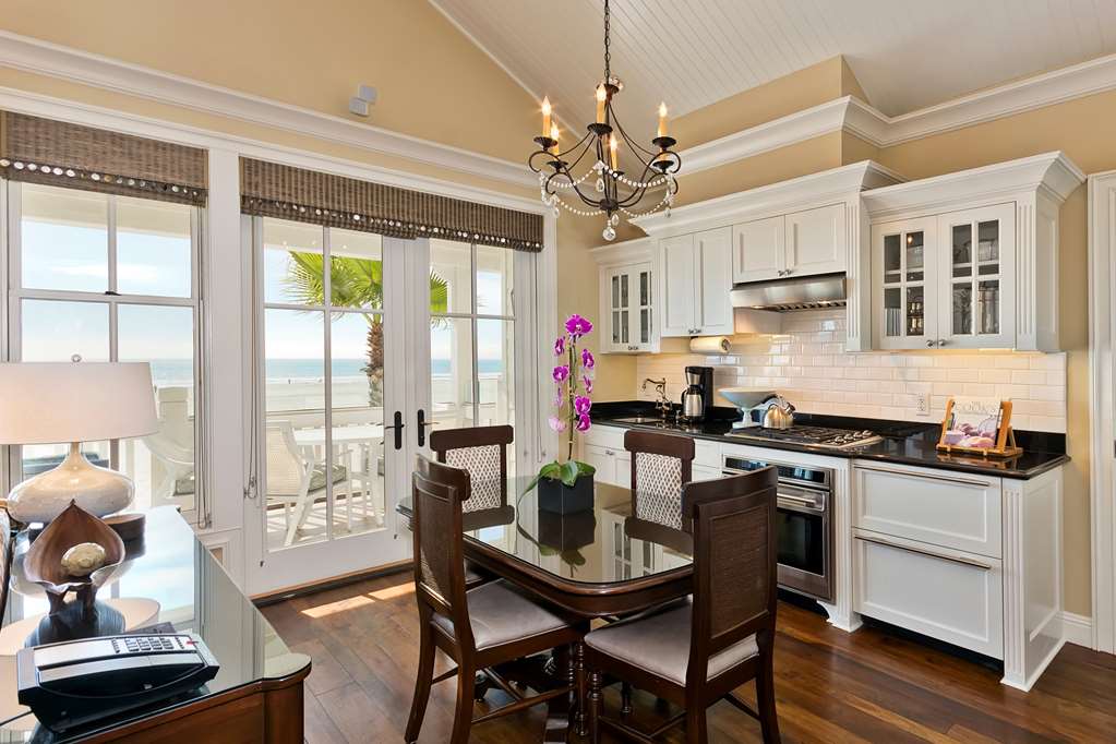 White kitchen with an island beside a dining table under a pendant light, doors onto the beach