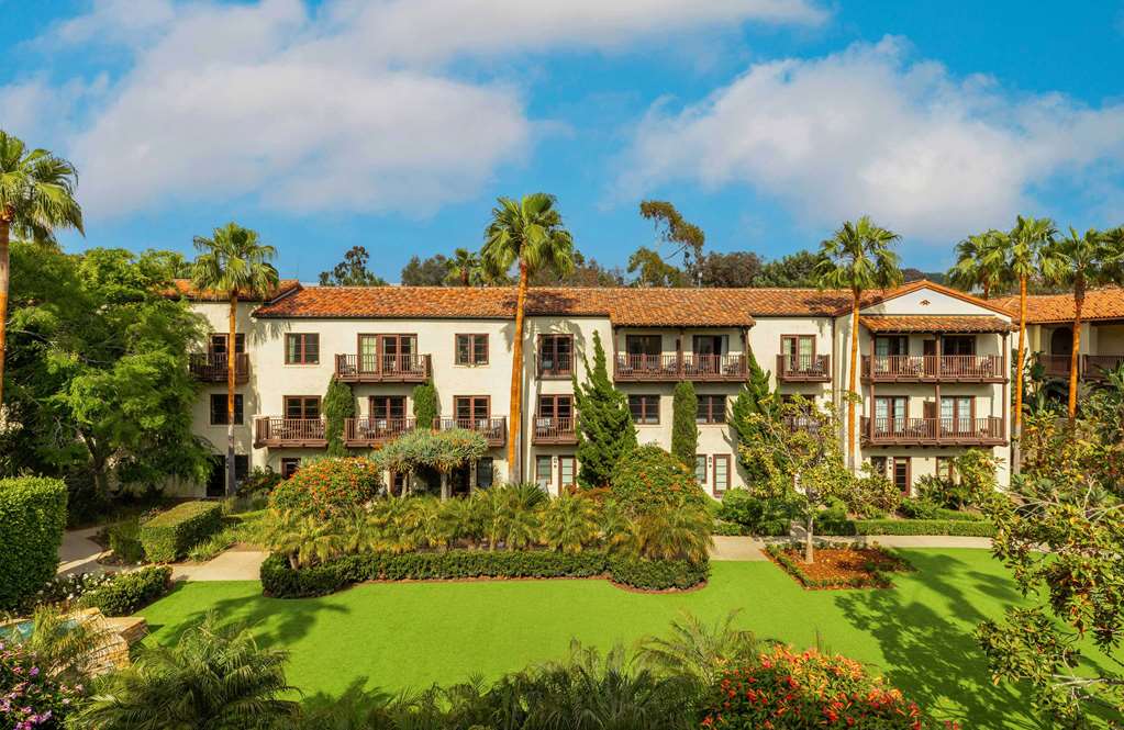 Three storey Spanish style buildings with red tile roofs around a lawn and palm trees
