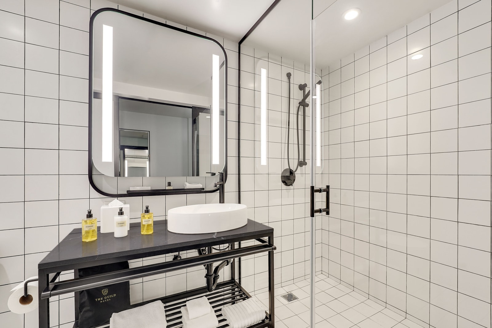 Bathroom interior with a black framed lit mirror, wall hung vanity and walk in shower alongside