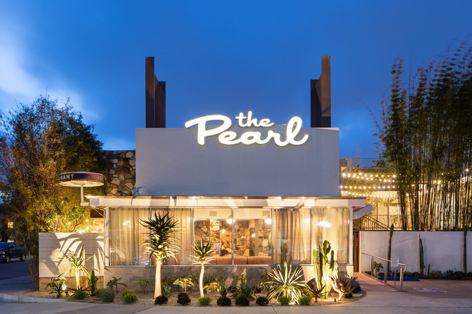 夜晚的旅館外觀，屋頂上一面手寫字體的 the Pearl 燈箱招牌，下方是低矮的白色量體與植栽