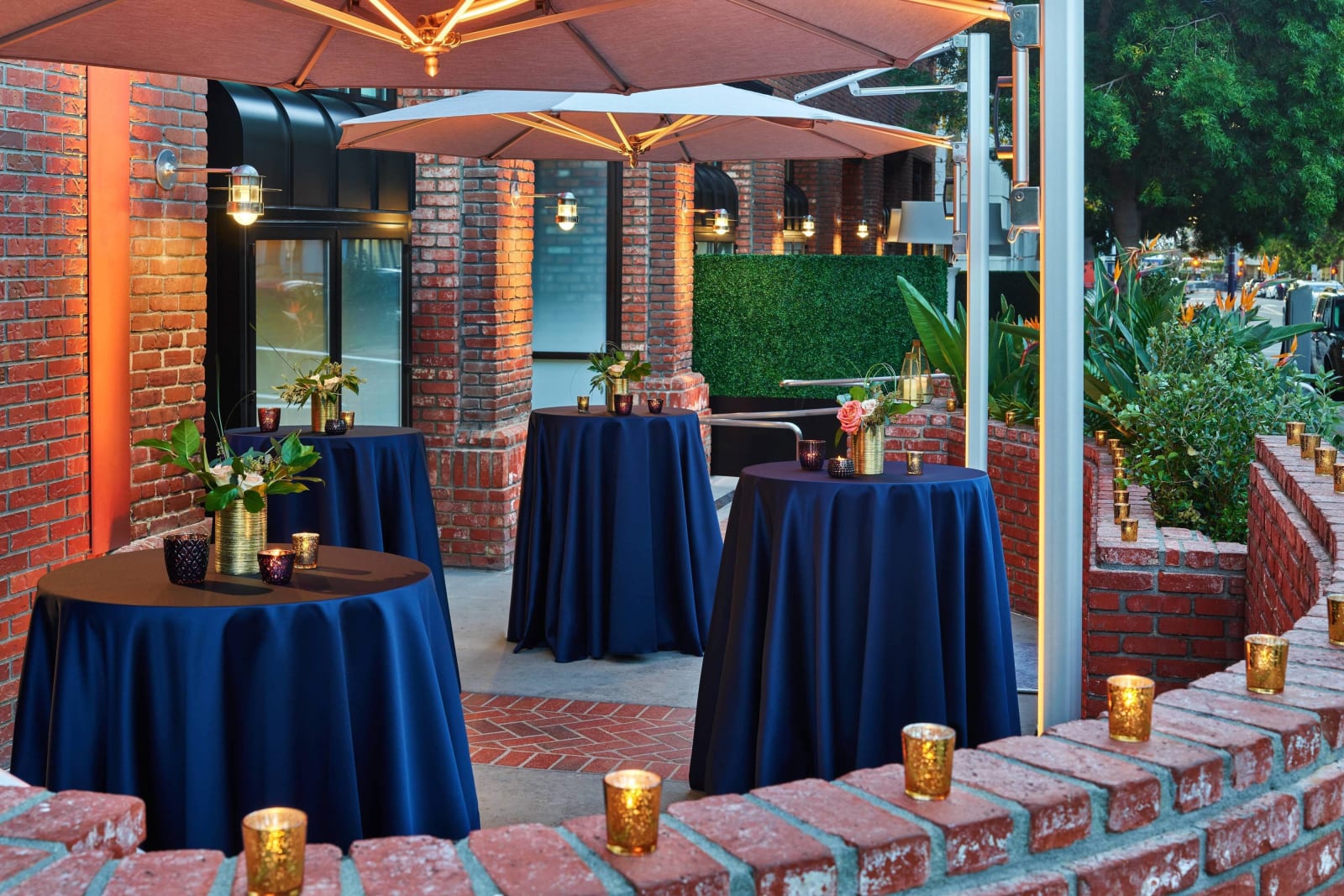 Outdoor courtyard enclosed by brick walls with blue draped cocktail tables and white umbrellas