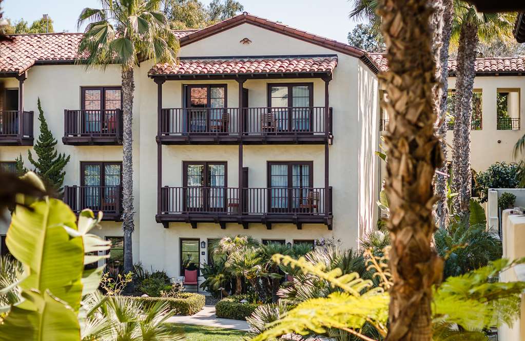 Three storey white building with timber railed balconies on every floor and palms in front