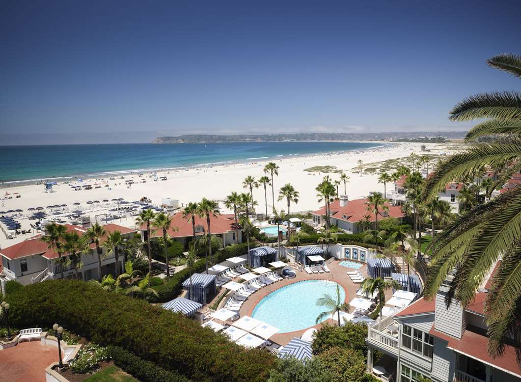 Aerial view over a field of palms and red roofs with the curve of the beach beyond