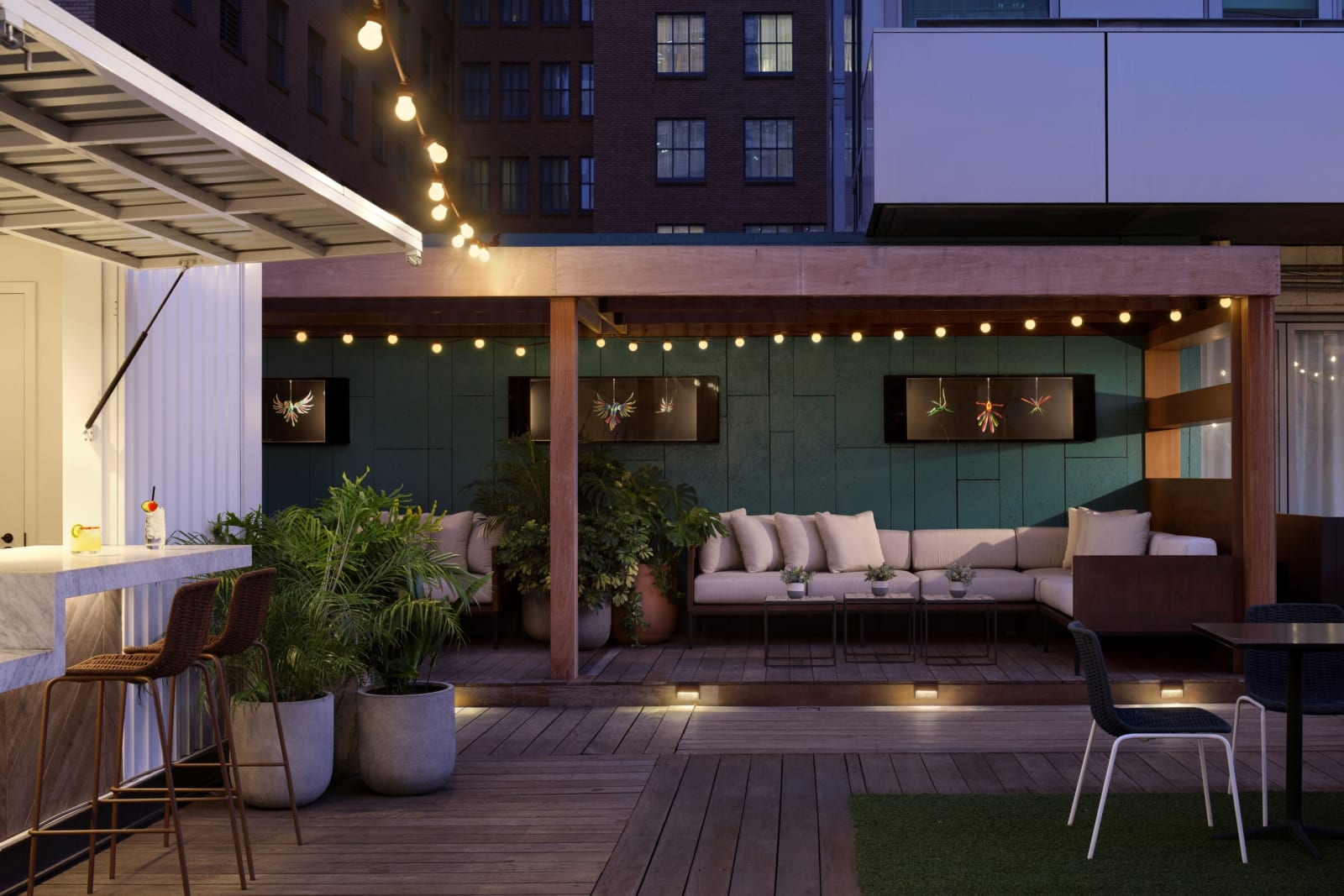 Rooftop terrace at night with a slatted timber pergola over a long banquette and warm string lights overhead
