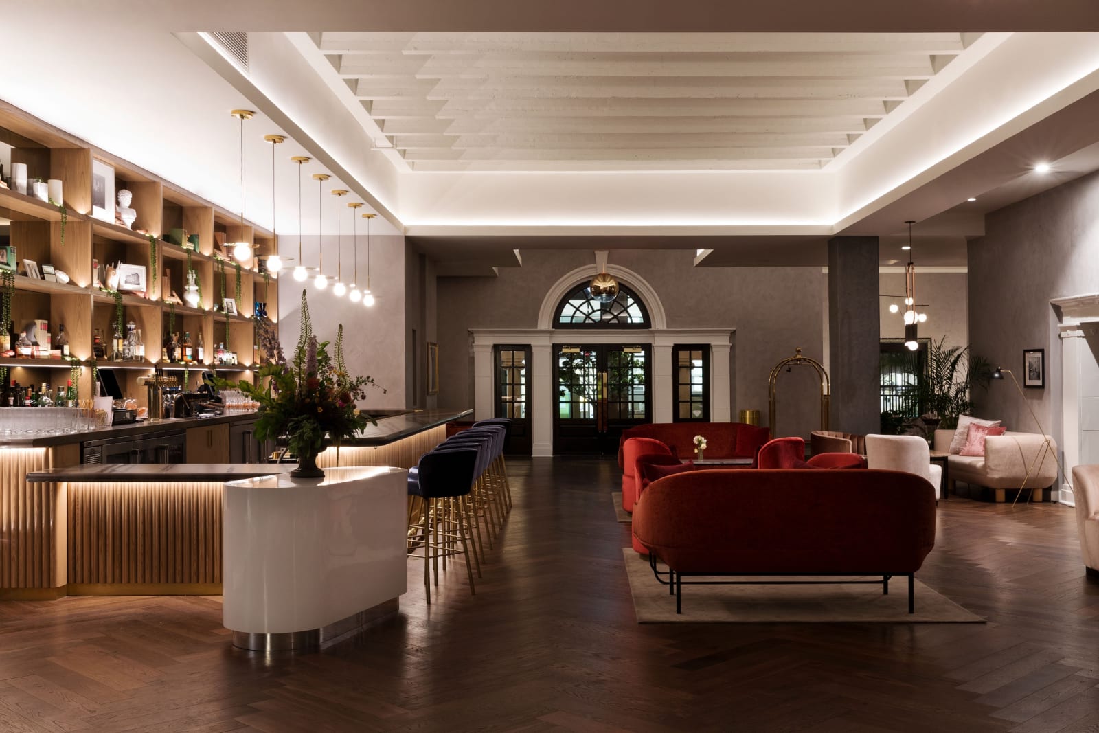 Lobby with a curved reception desk, a red velvet sofa, arches and shelving behind