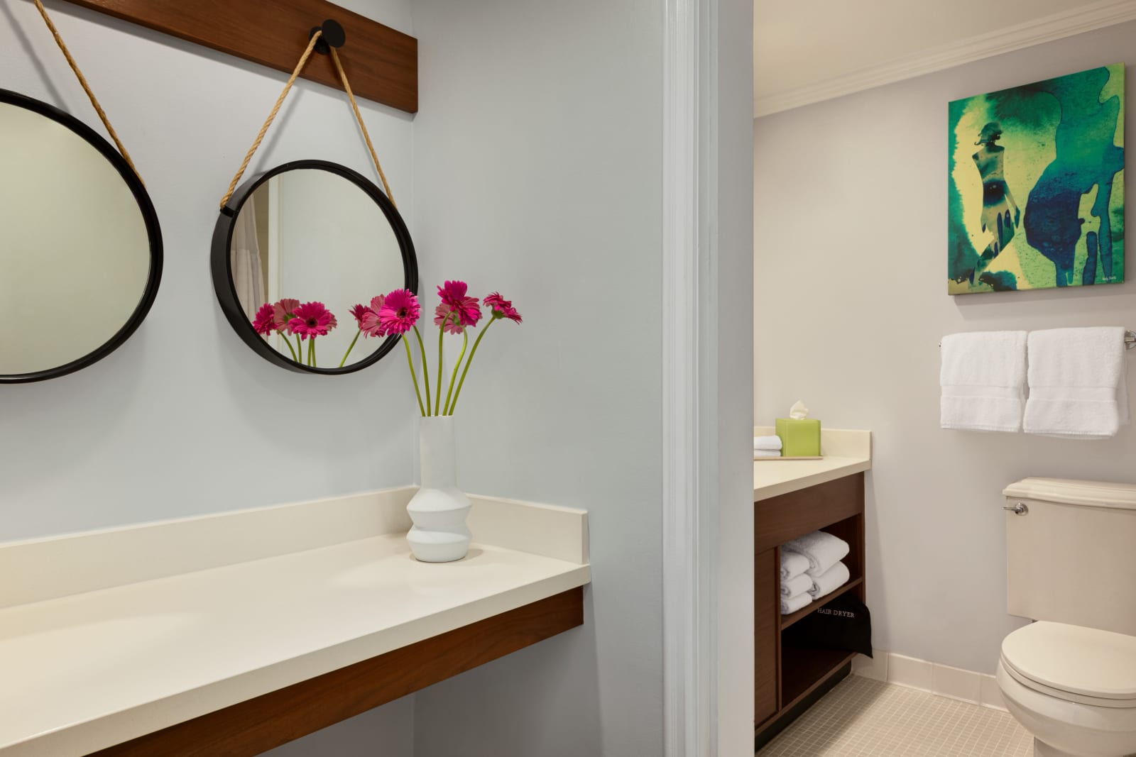 Bathroom with a round leather strap mirror, timber counter and a vase on the wall