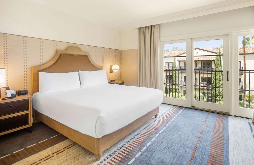 Guest room with a king bed and a full wall of french doors opening to a balcony over tile roofs