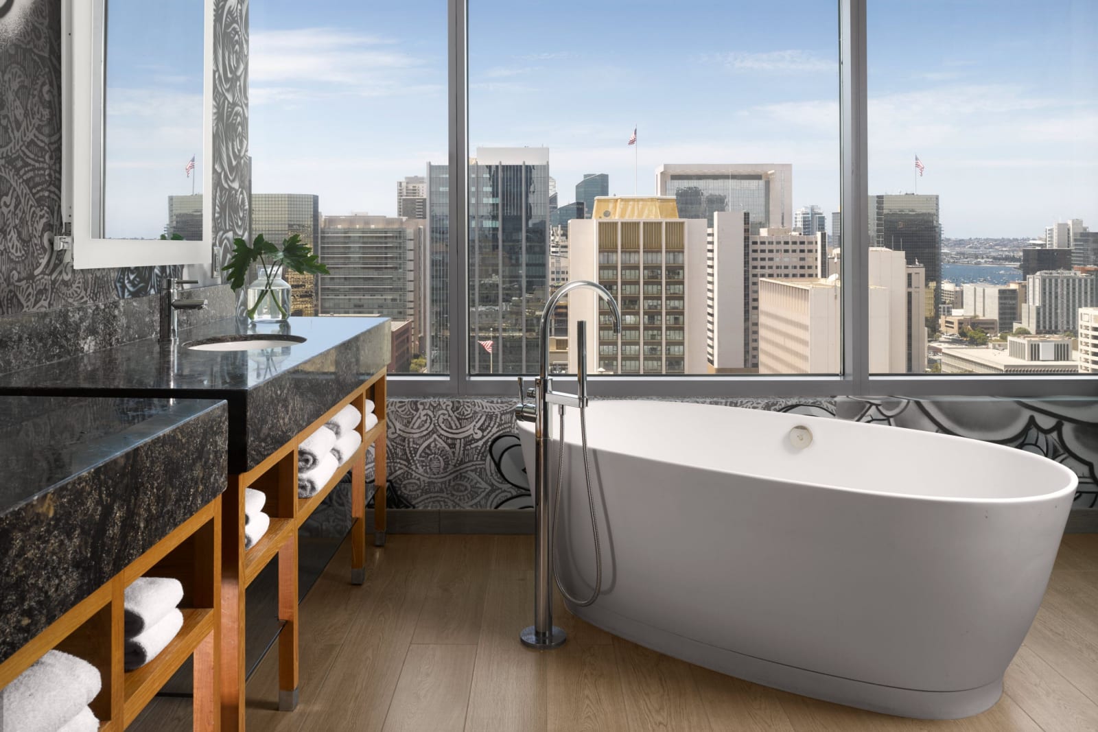 Suite bathroom with a freestanding tub set against a full height window looking out over the daytime city skyline